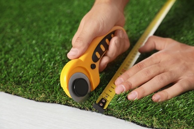 Man cutting artificial grass carpet indoors, closeup