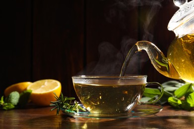 Pouring aromatic herbal tea into cup and rosemary on wooden table