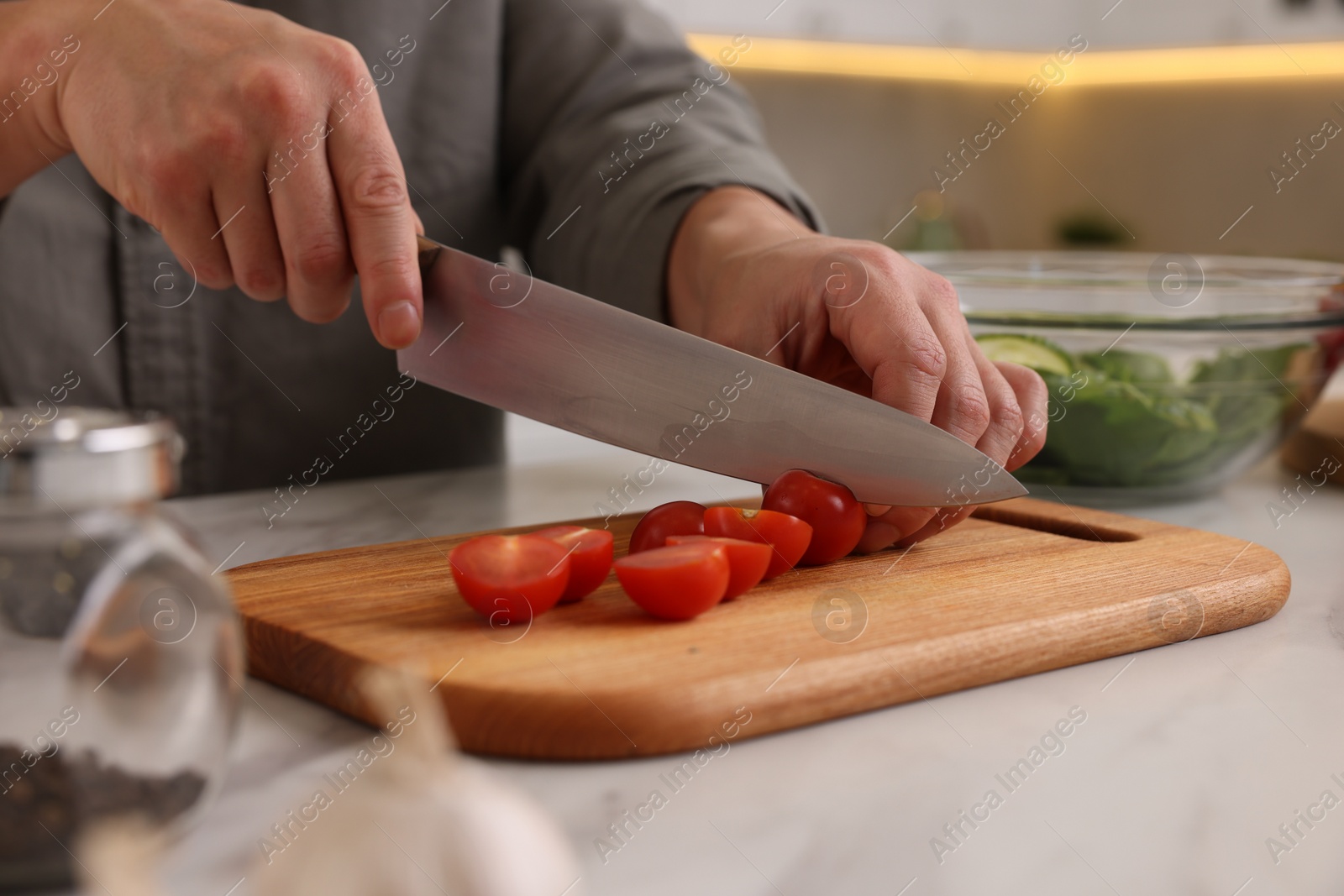 Photo of Cooking process. Man cutting fresh tomatoes at white marble countertop in kitchen, closeup