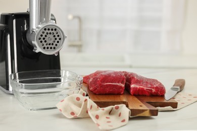 Photo of Electric meat grinder with beef and knife on white marble table in kitchen