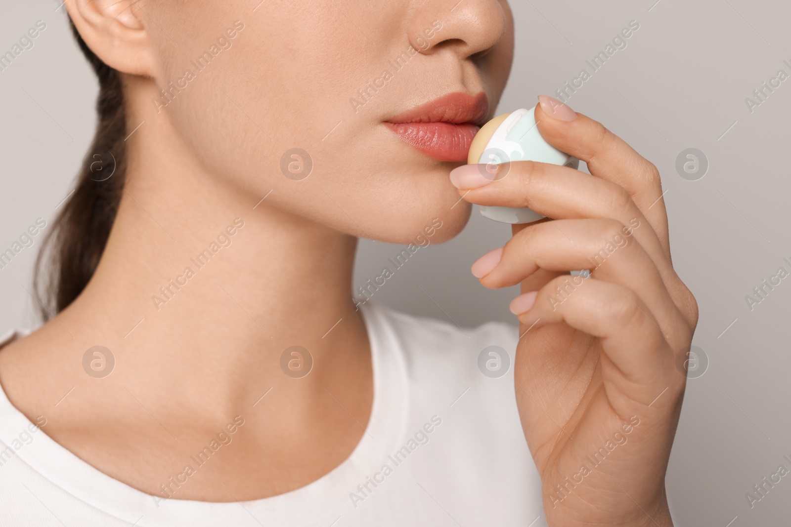 Photo of Young woman applying lip balm on grey background, closeup