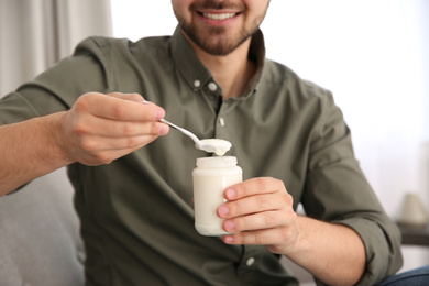 Photo of Young man with tasty yogurt indoors, closeup