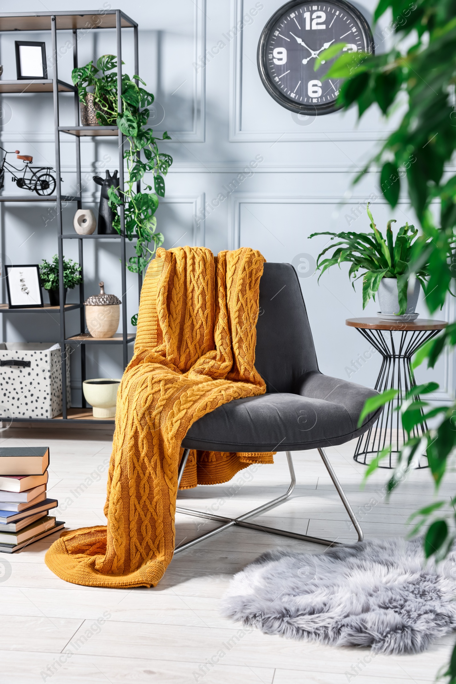 Photo of Comfortable armchair with blanket and houseplants in room