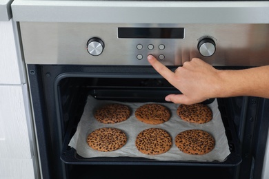 Photo of Young man baking cookies in oven at home, closeup