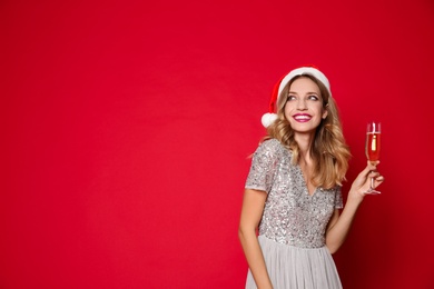 Photo of Happy woman in Santa hat with glass of champagne on red background, space for text. Christmas party
