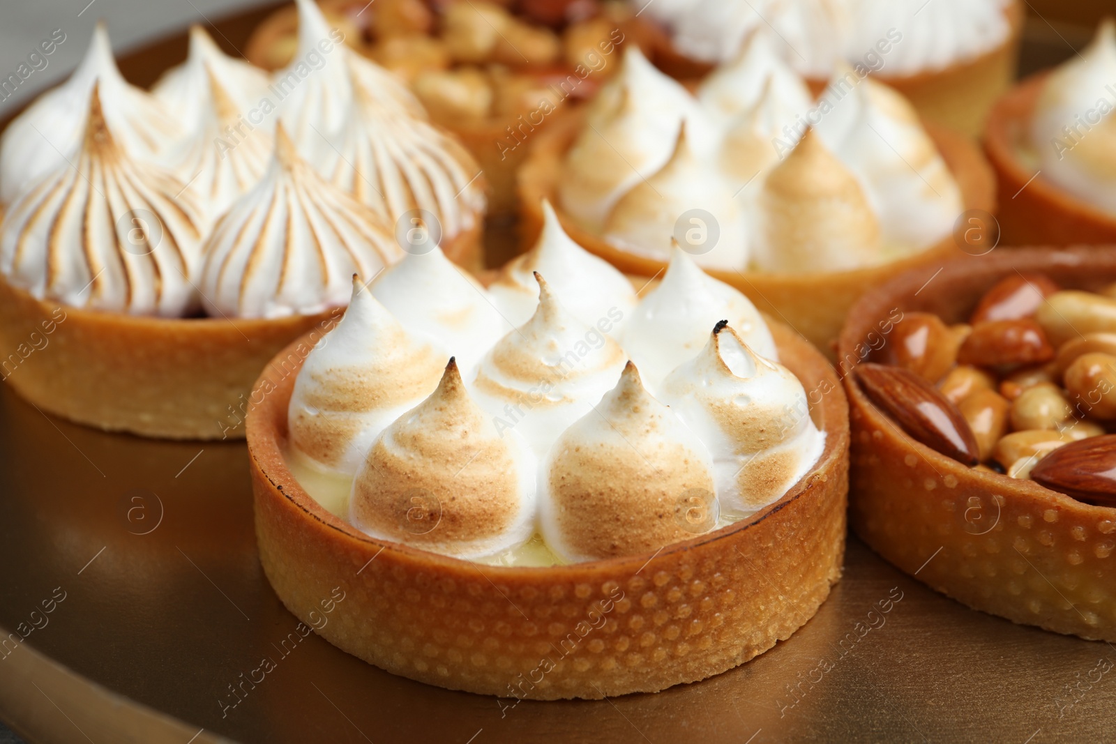 Photo of Many different tartlets on golden tray, closeup. Delicious dessert