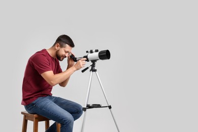 Photo of Astronomer looking at stars through telescope on light grey background. Space for text