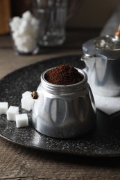 Photo of Ground coffee in moka pot and sugar cubes on wooden table, closeup