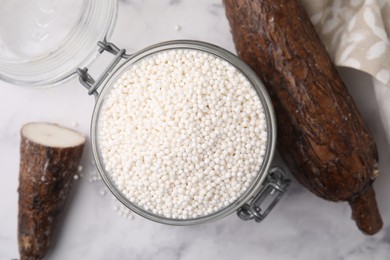 Tapioca pearls in jar and cassava roots on white table, flat lay