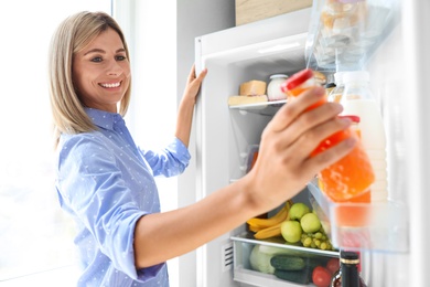 Woman taking bottle with juice out of refrigerator in kitchen