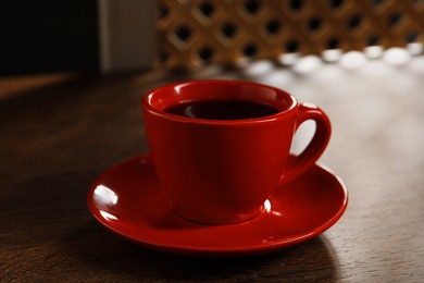 Red cup with aromatic coffee on wooden table indoors, closeup