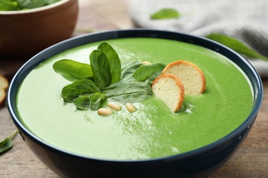 Photo of Bowl of healthy green soup with fresh spinach on wooden table, closeup view