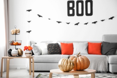 Photo of Modern room decorated for Halloween, focus on table with pumpkins. Festive interior