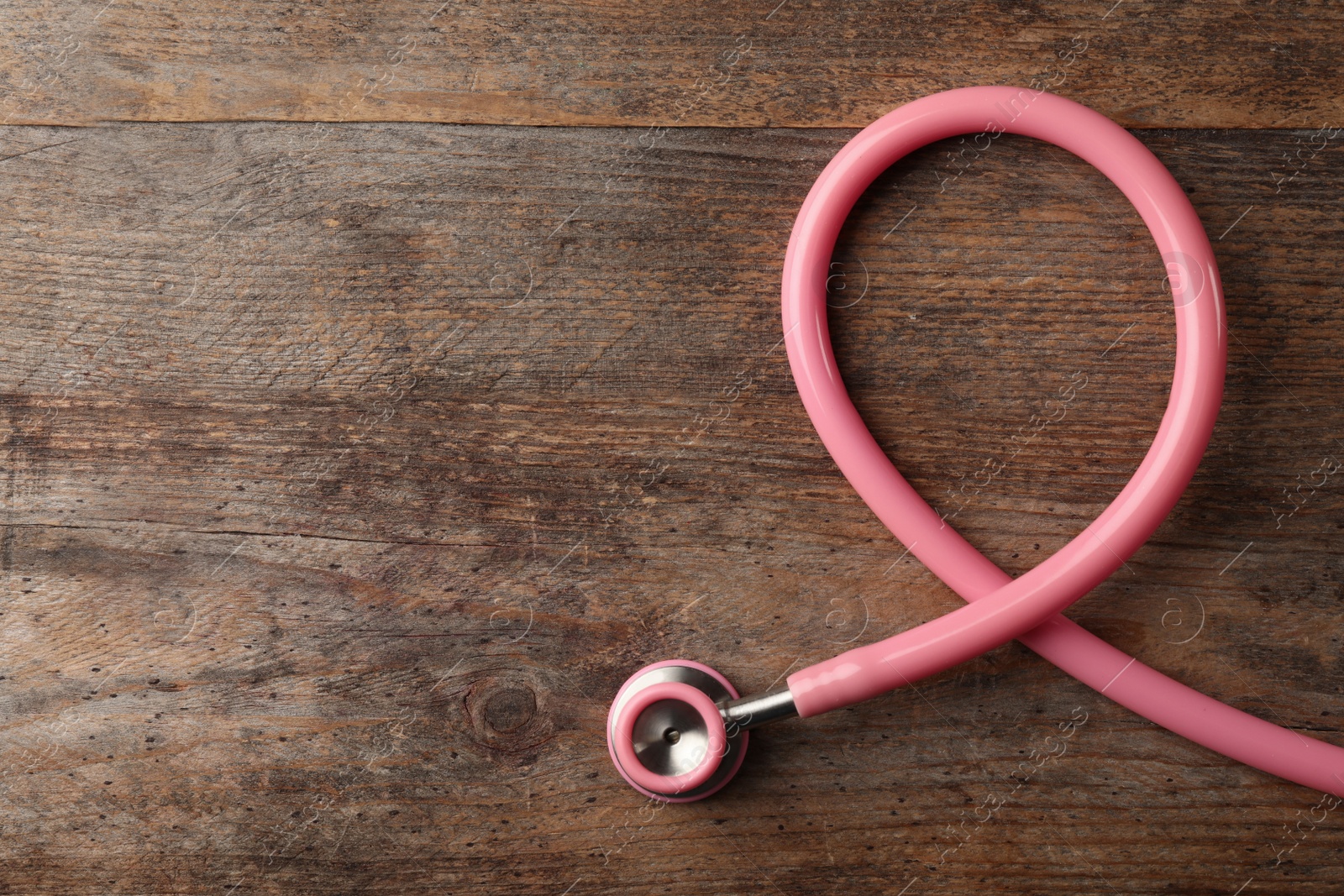 Photo of Pink stethoscope folded like awareness ribbon on wooden background, top view with space for text. Breast cancer concept