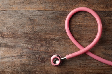 Pink stethoscope folded like awareness ribbon on wooden background, top view with space for text. Breast cancer concept