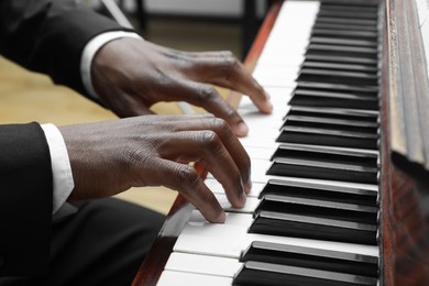 Photo of African-American man playing piano indoors, closeup. Talented musician