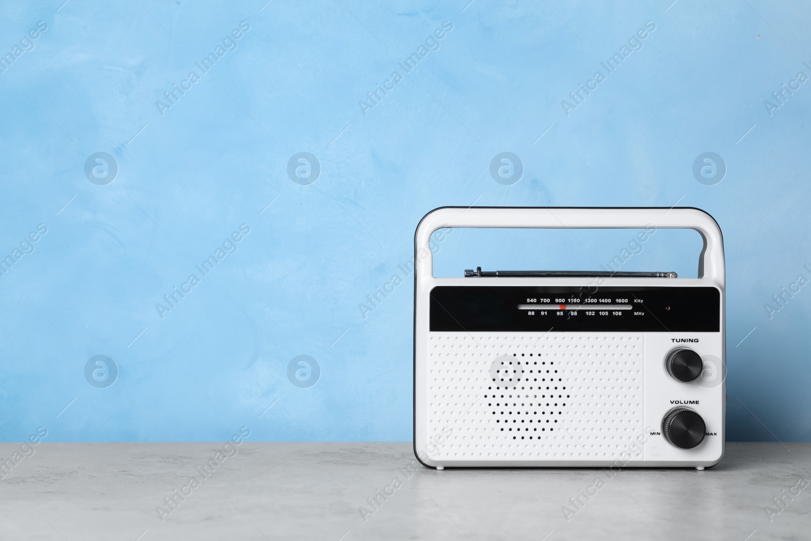 Photo of Retro radio receiver on grey table against light blue background. Space for text