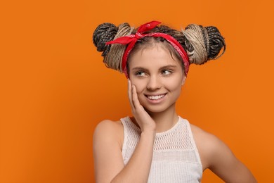 Beautiful woman with braided double buns on orange background, space for text