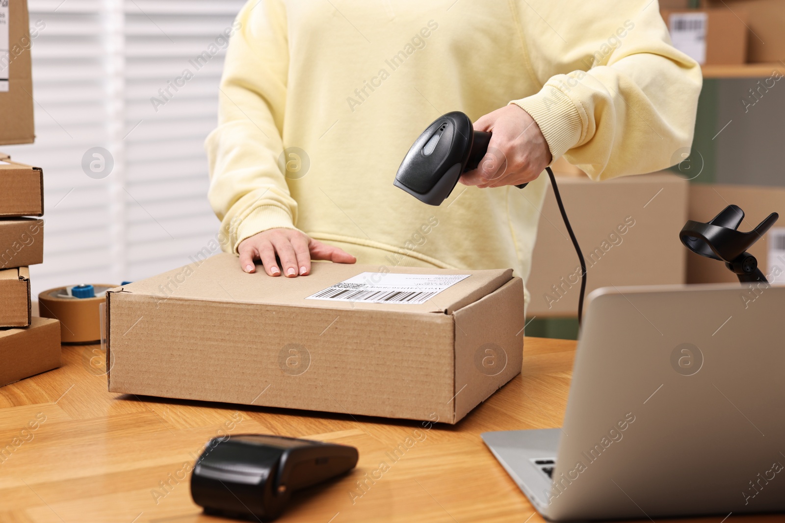 Photo of Parcel packing. Post office worker with scanner reading barcode indoors, closeup