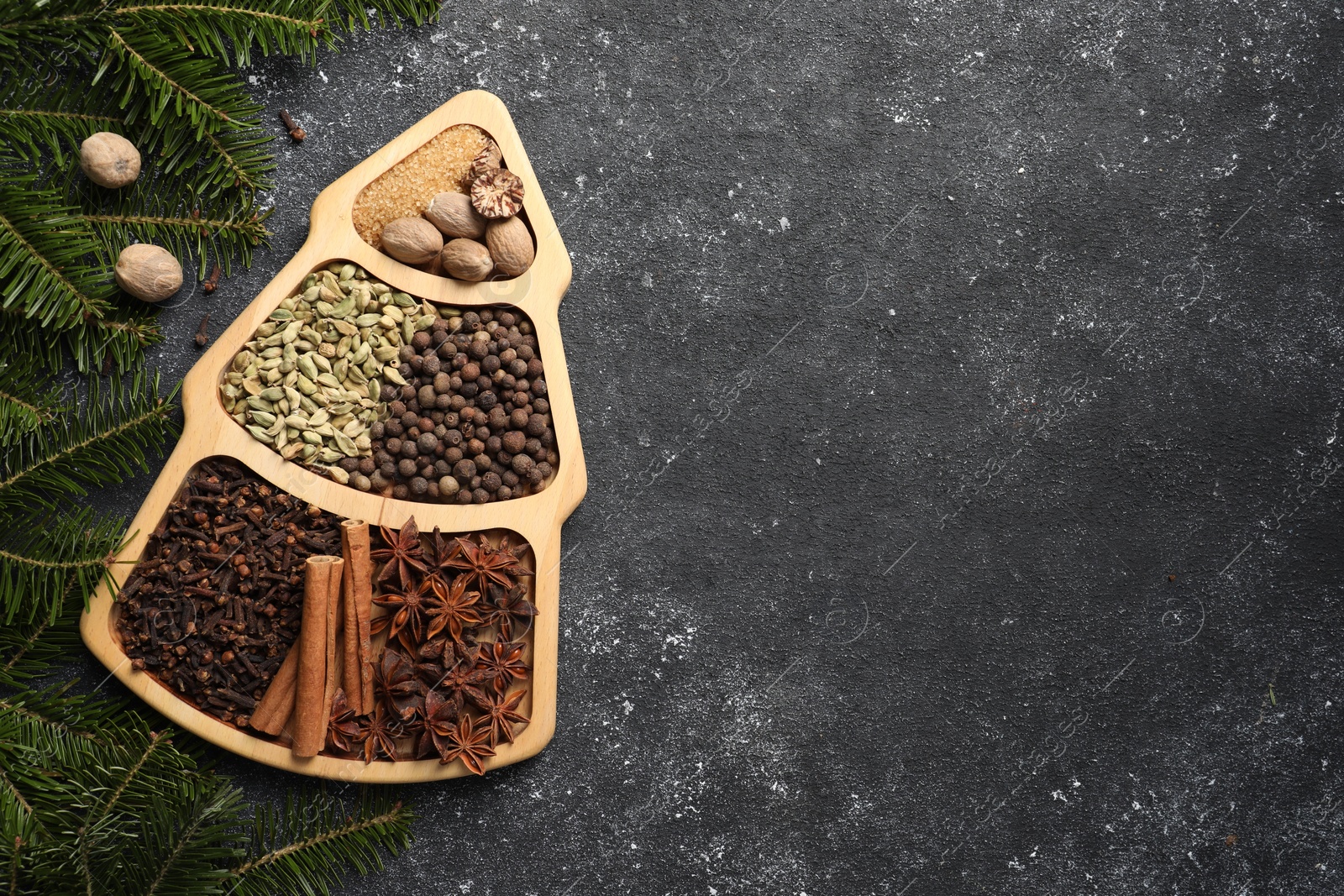 Photo of Different spices, nuts and fir branches on dark gray textured table, flat lay. Space for text