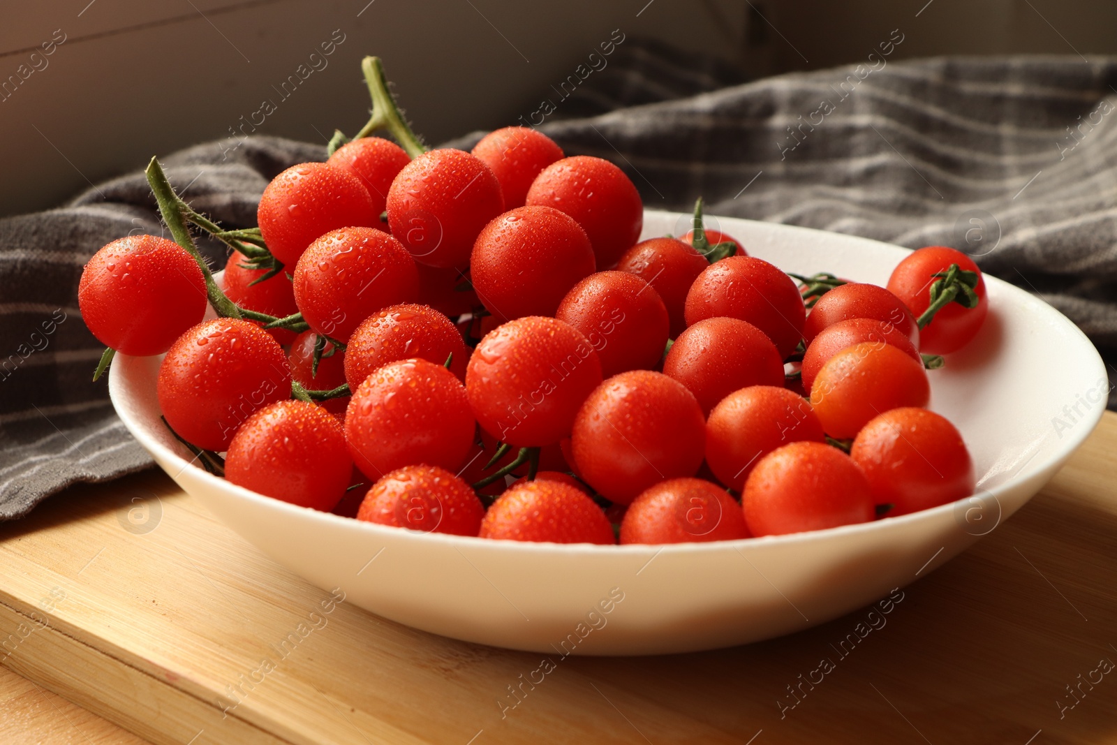 Photo of Plate of ripe whole cherry tomatoes with water drops on wooden table, closeup