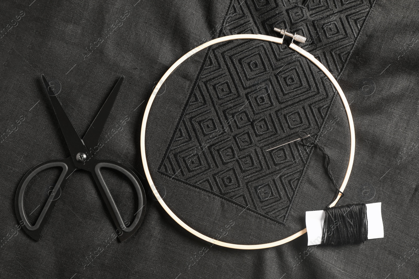 Photo of Embroidery hoop, thread and scissors on black shirt, flat lay. Ukrainian national clothes