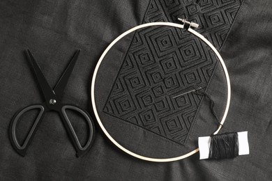 Photo of Embroidery hoop, thread and scissors on black shirt, flat lay. Ukrainian national clothes