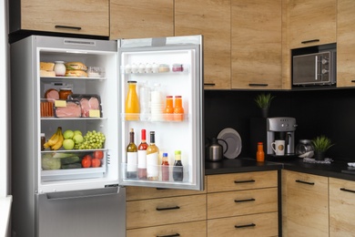 Photo of Open refrigerator full of products in kitchen