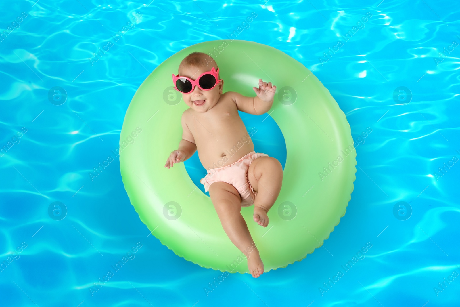 Image of Cute little baby with inflatable ring in swimming pool, top view