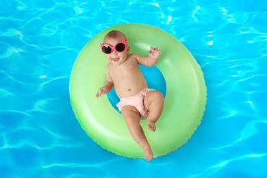 Cute little baby with inflatable ring in swimming pool, top view