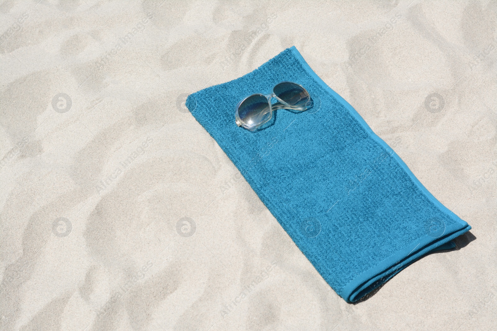 Photo of Soft blue towel and sunglasses on sandy beach, space for text
