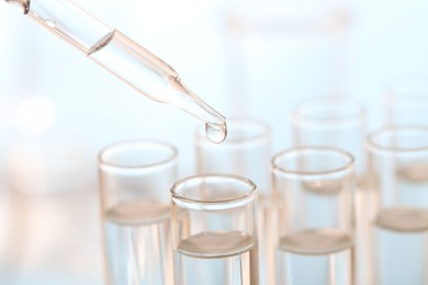 Photo of Laboratory analysis. Dripping liquid from pipette into glass test tube on blurred background, closeup