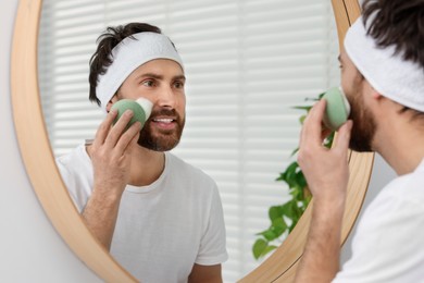 Man with headband washing his face using sponge near mirror in bathroom