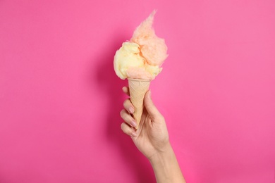 Photo of Woman holding ice cream cone with fluffy cotton candy on color background, closeup