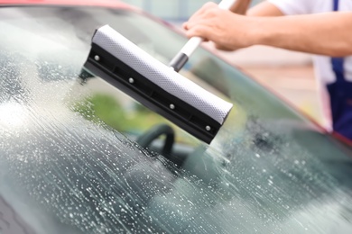 Photo of Man cleaning windshield with glass wiper, closeup. Car wash service