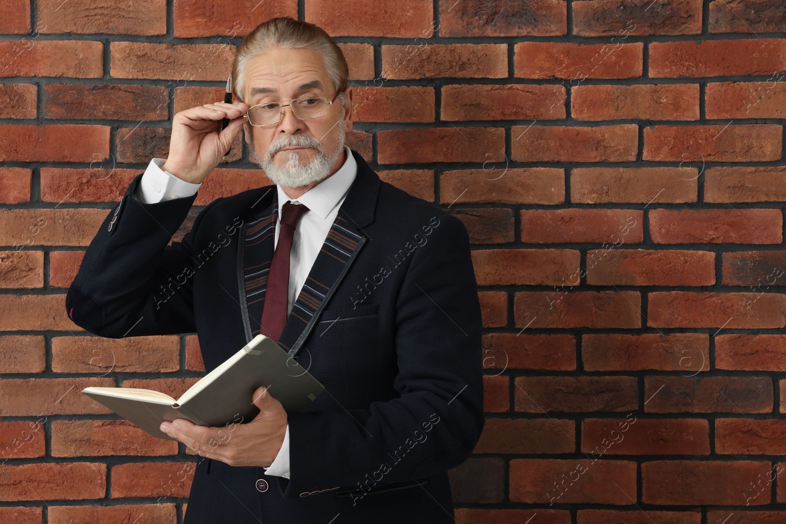 Photo of Serious senior boss in suit with notebook and pen near brick wall. Space for text