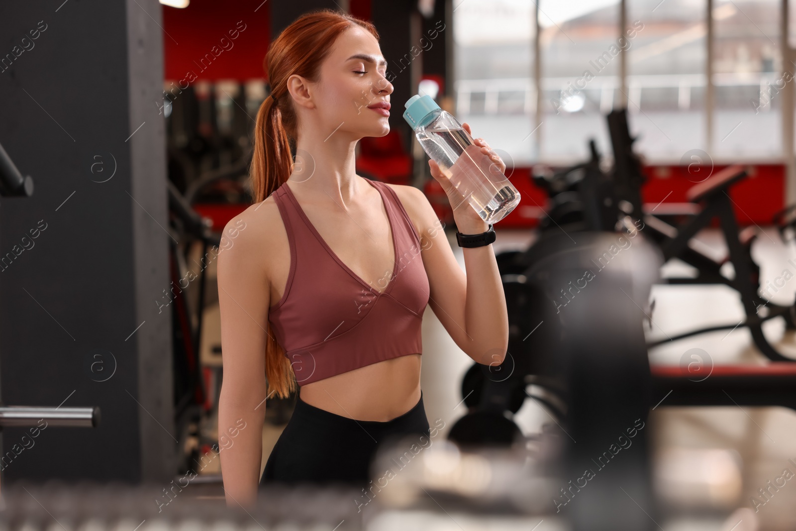 Photo of Athletic young woman with bottle of water in gym