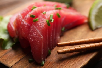 Tasty sashimi (pieces of fresh raw tuna with green onion) and chopsticks on wooden board, closeup