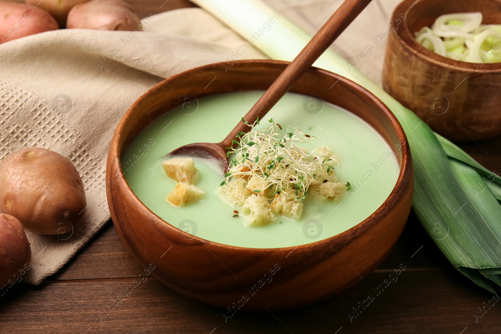 Photo of Bowl of tasty leek soup, spoon and ingredients on wooden table