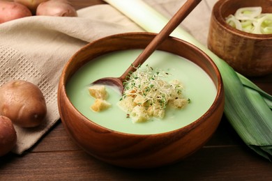 Photo of Bowl of tasty leek soup, spoon and ingredients on wooden table