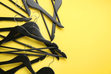 Black hangers on yellow background, flat lay. Space for text