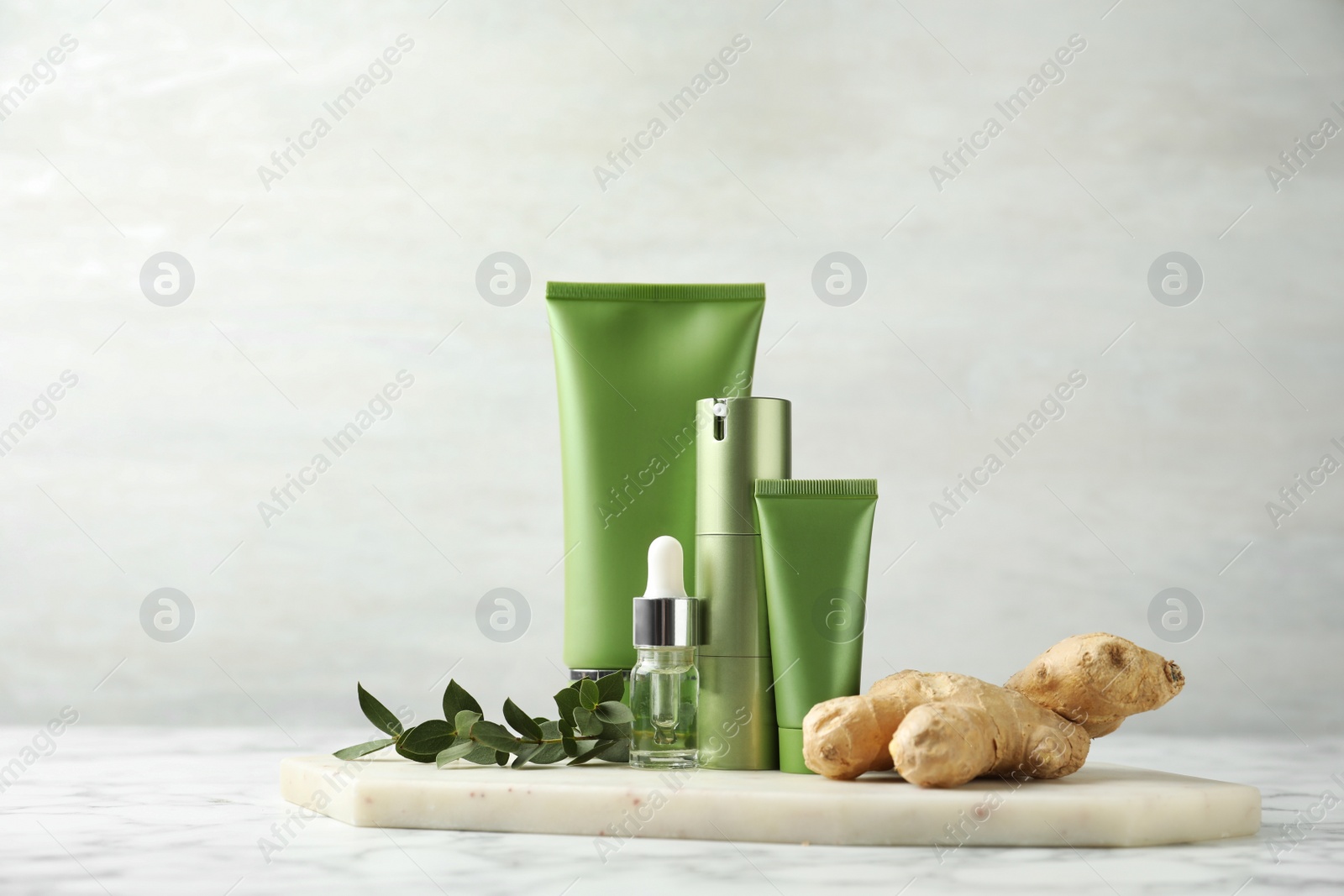 Photo of Set of cosmetic products, ginger and plant on white marble table