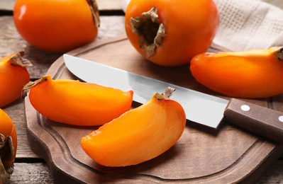 Photo of Delicious ripe persimmons and knife on wooden table