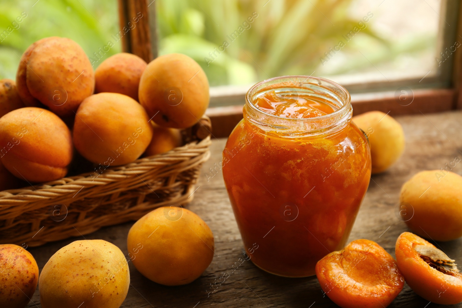 Photo of Jar of delicious jam and fresh ripe apricots on wooden table indoors. Fruit preserve