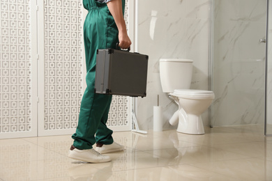 Professional plumber with toolbox near toilet bowl in bathroom, closeup