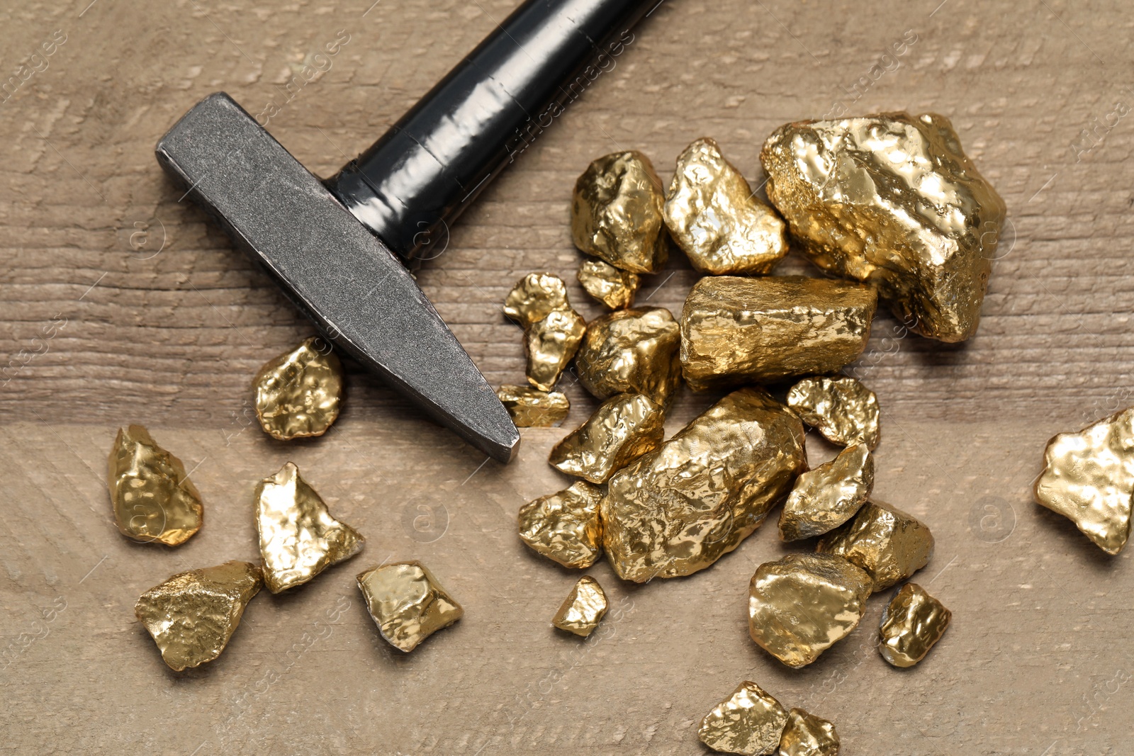 Photo of Pile of gold nuggets and hammer on wooden table, flat lay
