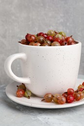 Photo of Cup with ripe gooseberries on light grey marble table