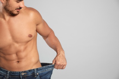 Young man with slim body in old big size jeans on grey background, closeup view. Space for text