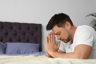 Handsome man saying bedtime prayer at home. Space for text