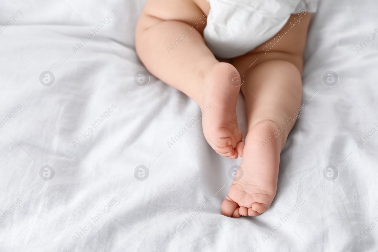 Photo of Cute little baby lying on bed, closeup of legs. Space for text